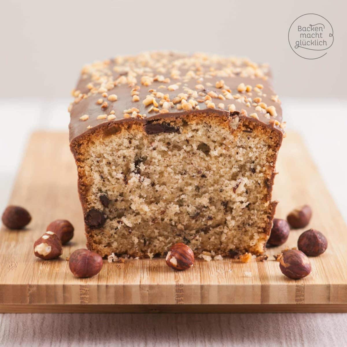 Angeschnittener Nusskuchen mit Schokoglasur und gehackten Haselnüssen auf Holzbrett