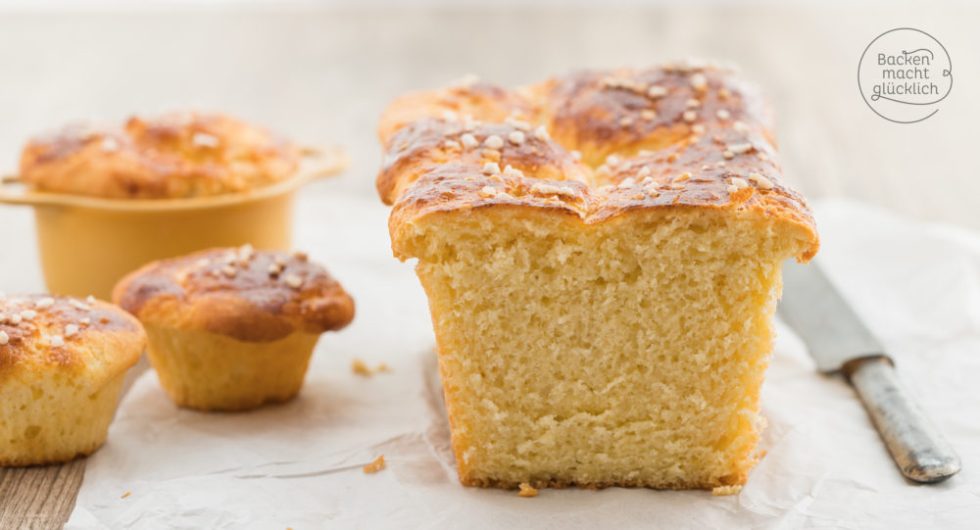 Angeschnittene Brioche zeigt lockere Krume, daneben kleine Brioche-Muffins mit Zuckerkruste