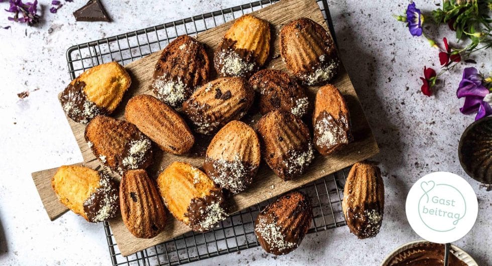 Madeleines mit Schokoladenüberzug und Kokosraspeln auf Holzbrett