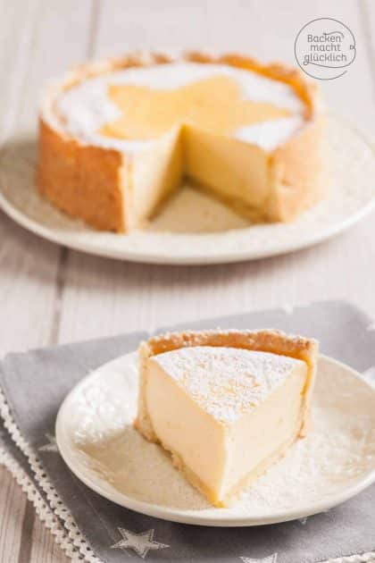 Angeschnittener Käsekuchen mit Mürbeteigboden, Tortenstück mit Puderzucker auf Teller