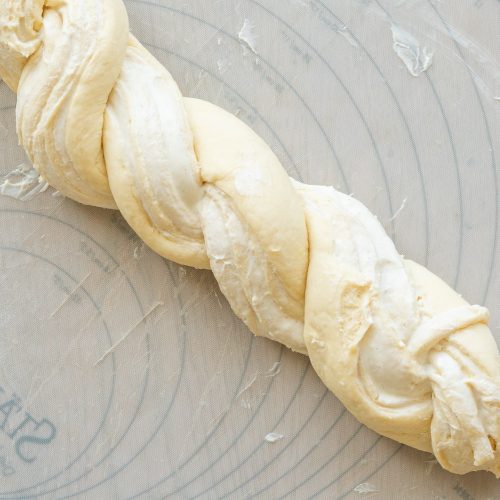 Geflochtener Hefezopf aus rohem Teig auf bemehlter Silikonmatte