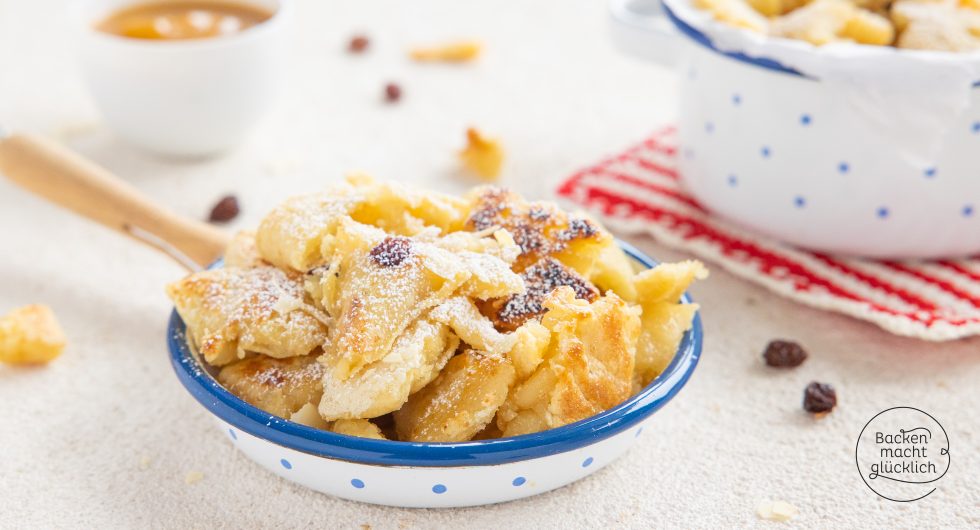Kaiserschmarrn mit Rosinen und Puderzucker im Emailleteller, Pfanne im Hintergrund
