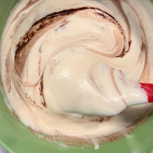 Marmorierter Kuchenteig mit Schokoladenschlieren wird in grüner Schüssel verrührt