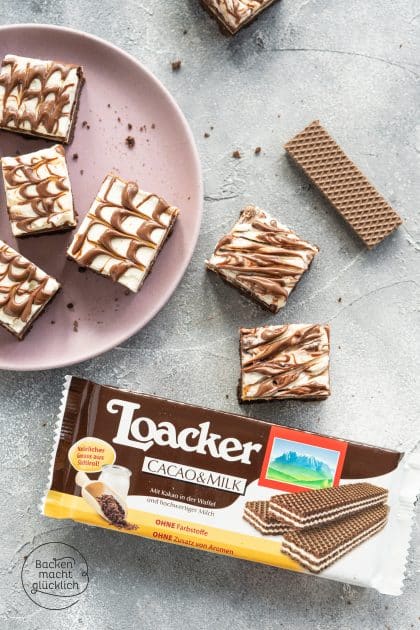 Schokoladige Cheesecake-Würfel mit Marmormuster auf rosa Teller neben Loacker-Waffeln