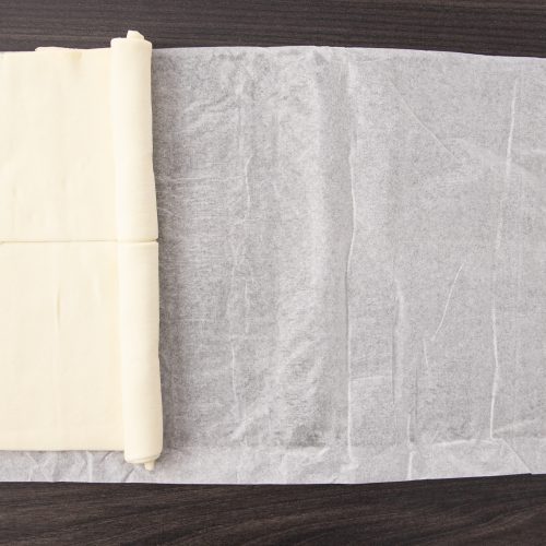 Ausgerollter Blätterteig auf Backpapier, teilweise zu Rolle aufgewickelt