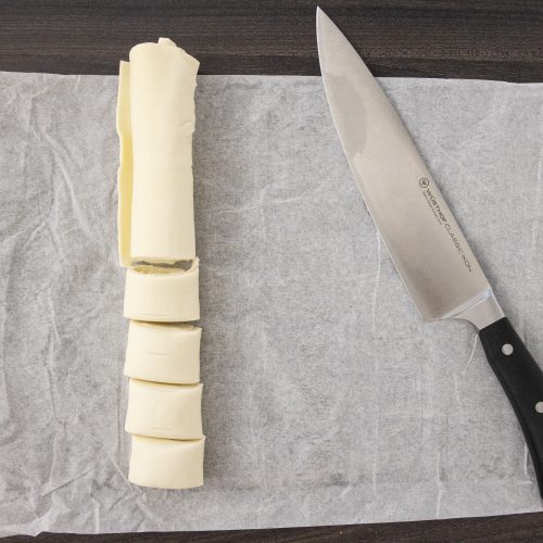 In Scheiben geschnittene Butterrolle neben Kochmesser auf Backpapier