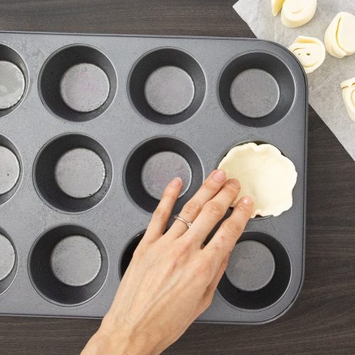 Teigrolle wird in Muffinform gedrückt, weitere Teigröllchen liegen bereit