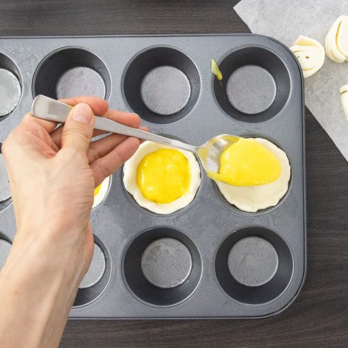 Eiercreme wird mit Löffel in Blätterteigförmchen der Muffinform gefüllt