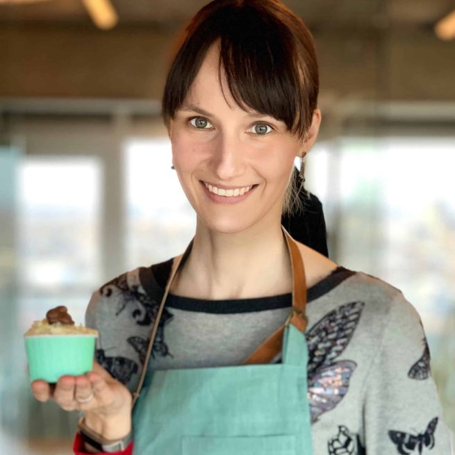 Lächelnde Frau mit türkiser Schürze hält Cupcake mit Schokoladentopping in der Hand