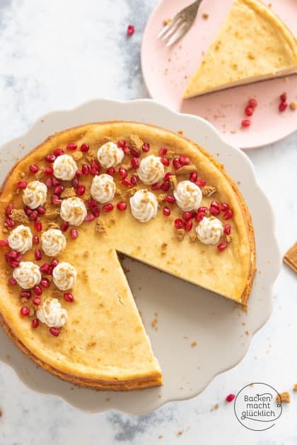 Angeschnittener Spekulatius-Cheesecake mit Sahnetupfen und Granatapfelkernen, ein Stück daneben serviert
