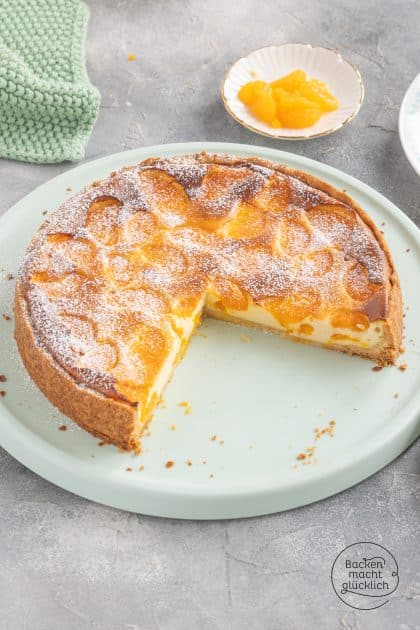 Angeschnittener Mandarinen-Käsekuchen mit Puderzucker bestäubt auf grünem Teller