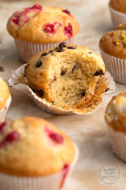 Angebissener Schokoladen-Muffin zeigt lockere Krume, umgeben von Himbeer- und Pistazienmuffins