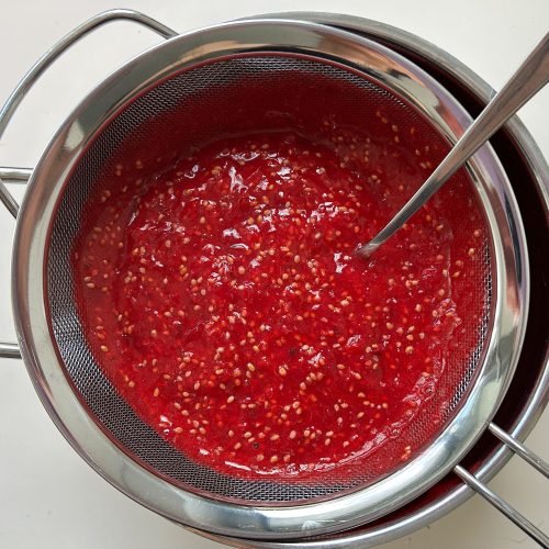 Pürierte Johannisbeeren im Sieb, Löffel streicht Kerne ab