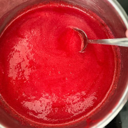 Rote Johannisbeermarmelade köchelt im Topf, wird mit Löffel umgerührt