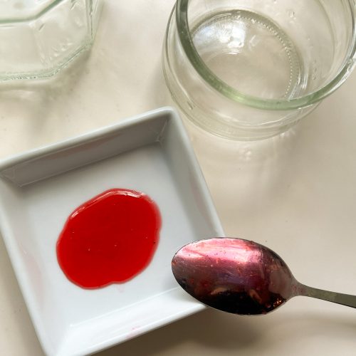 Geliertest der Johannisbeermarmelade auf Teller, leere Einmachgläser daneben