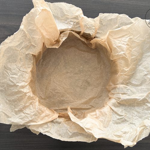 Mit zerknittertem Backpapier ausgelegte runde Springform für Käsekuchen