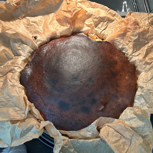 Baskischer Käsekuchen mit dunkel karamellisierter Oberfläche in Backpapier, frisch aus dem Ofen