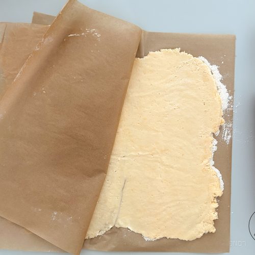 Ausgerollter Hefeteig zwischen Backpapier, rotes Nudelholz daneben