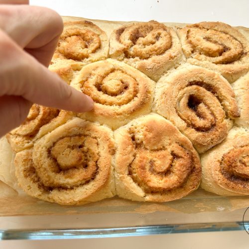 Hand zeigt auf frisch gebackene glutenfreie Zimtschnecken in Auflaufform
