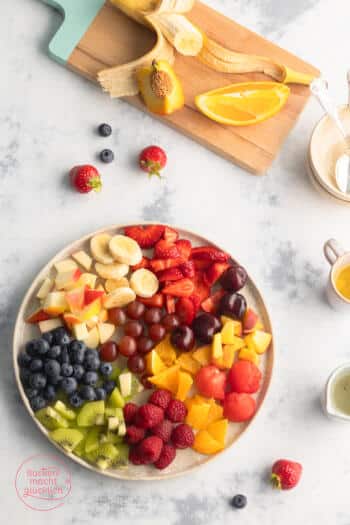 Obstsalat vorbereiten aus Beeren, Banane, Apfel, Orange und Pfirsich